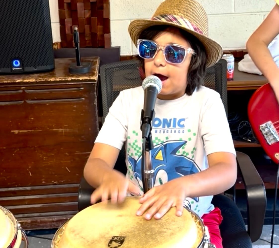 Child singing into microphone playing drum